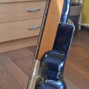 Detailní pohled na tělo a hmatník elektrické kytary v černé barvě s vysokým leskem. Hmatník je vyroben ze světlého dřeva. Nástroj je umístěn v černém…
