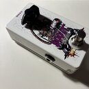 Bílý kytarový efekt pedál s grafickým motivem v centerX. Na horní straně je nápis BOOST a menší texty Gain a IR-Xaxis. Na boku je vidět vstupní konek…