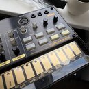 Černý sekvenční syntezátor s oranžovými nápisy KORG a volca beats. Zařízení obsahuje řadu bílých tlačítek, šedé otočné knoflíky a spodní sekci s žlut…