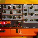 Červený syntetizátor s nápisem VIRTUAL ANALOG SYNTHESIZER. Panel obsahuje numeroustovací knoflíky, posuvníky a tlačítka s označením sekcí LFO 1, LFO…