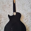 Zadní strana černé elektrické kytary s tvarem typu Les Paul. Na zadní části krku je viditelná rozsáhlá oprava nebo slep v béžové barvě. Tělo má v dol…