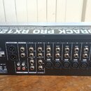 Zadní strana černého rackového zařízení s bílými nápisy. Na horní části je velký nápis EURORACK PRO RX1202FX a text ULTRA LOW-NOISE DESIGN 12-INPUT M…