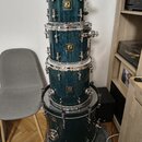 Čtyři tmavě modré bubny s texturovaným povrchem naskládané na sebe. Každý buben má na přední straně zlatý čtvercový štítek s nápisem SONOR Drums. Kov…
