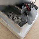Detail stříbrného kovového šasi s vnitřními komponenty a pružinou. Na spodní části je nalepený štítek s nápisem Products of Roland JAPAN a číslem 634…