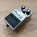 Stříbrný efekt pedál s černým gumovým spínacím tlačítkem. Na horní části je nápis FUZZ, model FZ-5, logo BOSS a označení COSM. Pedál má dva ovládací…