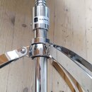 Detail chromovaného stojanu bubeníka s černým sedákem. Na středovém sloupku je viditelný nápis MAPEX a pod ním menší, nečitelný text. Povrch chromu j…