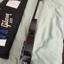 Černá elektrická kytara s tmavým hmatníkem, položená vedle černého obalu. Na obalu je bílý nápis Gibson USA. Kytara má na spodní části těla vstupní j…