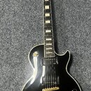 Černá elektrická kytara s tvarem Les Paul a bílým lemováním hran. Na hlavě je viditelné logo Epiphone a zlaté ladičky. Nástroj má dva humbuckery, zla…