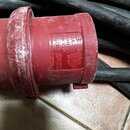 Červený plastový průmyslový konektor s připojeným černým kabelem. Na povrchu je vyražen nápis „32A-6h / 200-415V“, „3P+N+PE IP44“, „Typ: 214“ a „Made…