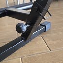 Detail černé kovové konstrukce s nastavitelným výškovým mechanismem. Jsou vidět otvory pro zajištění výšky a kovový pružinový čep. Na konstrukci je u…