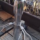 Chromovaný kovový stojan s teleskopickým mechanismem a knurlovaným nastavovacím knoflíkem. Na středové noze je viditelné malé kulaté logo s písmenem…