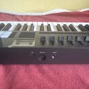 Černý MIDI kontrolér s klávesnicí a řadou ovládacích posuvníků. Na zadní straně jsou viditelné konektory s nápisy USB, MIDI Out a Sustain. Na horním…