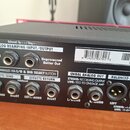 Zadní strana černého elektronického zařízení s řadou konektorů a popisnými štítky. Jsou zde nápisy „ANALOG REAMPING INPUT/OUTPUT“ s vstupy „Line Leve…