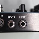 Detail zadní strany černého elektronického zařízení s kovovým broušeným panelem. Jsou zde tři konektory s bílými nápisy: MIDI IN (5pinový DIN), INPUT…