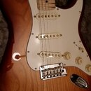 Elektrická kytara s trupem v hnědém sunburst provedení a bílým pickguardem. Nástroj má tři bílé snímače typu single-coil a chromovaný kobylník. Hmatn…