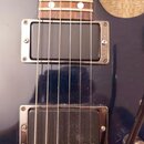 Detail elektrické kytary v tmavě modré barvě s hnědým hmatníkem. Nástroj má dva humbuckery s chromovanými rámečky, přičemž na spodním snímači je bílý…
