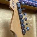 Zadní strana hlavy kytary z přírodního dřeva s šesti kovovými ladičkami. Na dřevě je vidět logo ve tvaru trojúhelníku s nápisy „Custom Shop“ a „Fende…