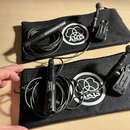 Dvě černé zipové pouzdra s bílým logem AKG. V každém pouzdře je černý mikrofon s připojeným kabelem a držákem. Na spodním mikrofonu je nápis PHANTOM…