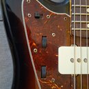 Detail elektrické basy s černým lakem přecházejícím do hnědé. Nástroj má hnědý pickguard s texturou želvy a bílé kryty snímačů. Na povrchu jsou vidět…