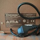 Detail zadní strany hnědého komba s texturovaným povrchem. Na černém štítku je uveden MODEL ACOUSTASONIC™, INPUT 230V~50Hz a POWER 35W. Dále je uvede…