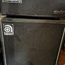 Černý basový zesilovač a reproduktorová skříň. Na horním přístroji je nápis Heritage SVT-CL, logo Ampeg a nápis Heritage. Spodní skříň má v horní čás…