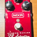 Červený kytarový efekt s nápisy MXR, CUSTOM BADASS a '78 distortion. Na horní straně jsou tři černé otočné knoflíky s popisky CRUNCH, TONE a DISTURTI…