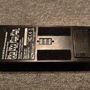 Spodní strana černého expresního pedálu s dvěma velkými velcro pásy. Na spodní straně je bílý štítek s nápisy SOURCE AUDIO, SA183 REFLEX Universal Ex…