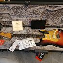 Elektrická kytara typu Stratocaster v barevném přechodu od žluté přes červenou k černé, s bílým pickguardem a třemi zlatými snímači. Na hlavě hmatník…