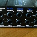 Černý kovový přístroj s řadou jackových konektorů. Na horní části jsou nápisy „Splitter—“, „INPUT“, „FOUR OUTPUT“, „THREE OUTPUT“, „TWO OUTPUT“ a „ON…