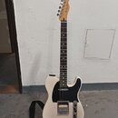 Bílá elektrická kytara s černým pickguardem a hnědým hmatníkem. Na hlavě je viditelné logo Fender. Nástroj má jeden humbucker v pozici mostu a jeden…