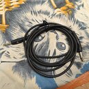 Černý instrumentální kabel s konektory typu 6,35 mm jack na obou koncích. Na levém konektoru je viditelné malé kulaté logo ve zlaté barvě. Kabel je s…