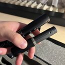 Ruka drží dvě černé komponenty mikrofonu. Na horní části je viditelný nápis SENNHEISER s logem značky. Na spodní části je nápis SENNHEISER KOPR a log…