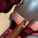 Detailní pohled na spoj hnedebního nástroje, pravděpodobně akustické kytary, s korpusem. Nástroj má tmavě hnědý dřevěný povrch a na boku korpusu jsou…