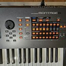 Černý digitální syntezátor s bílými a černými klávesami. Na horním panelu je nápis MUSIC SYNTHESIZER a výrazné logo MONTAGE 5. Ovládací panel obsahuj…