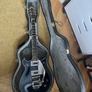 Tmavě modrá elektrická kytara v černém tvrdém kufru s šedým vnitřkem. Na hlavě nástroje je bílý nápis GRETSCH a na těle je viditelné logo Gretsch. Ky…