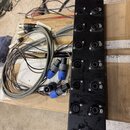 Černý kovový panel s řadou konektorů, vedle kterého leží několik šedých a černých kabelů s modrými konektory. Panel obsahuje deset dvojic konektorů,…