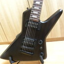 Černá elektrická kytara s ostře hranatým korpusem a hnědým hmatníkem. Nástroj má dva humbuckery, jeden ovládací potenciometr a přepínač. Povrch korpu…