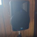 Černý aktivní reproduktor umístěný na kovovém stativu. V pravém dolním rohu je vidět nápis OPERA a pod ním logo Turbosound. Povrch je z černého plast…