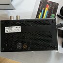 Černý kovový přístroj s perforovaným zadním panelem a napájecím kabelem. Na bílém štítku jsou nápisy TouchMonitor, RTW, P/N TM3-3GS, S/N 1169 a CE. D…