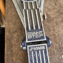 Detailní pohled na pedál basového pedálu v modré barvě s kovovými prvky. Na horní části je nápis GIANT STEP a na spodní části nápis SONOR s doprovodn…