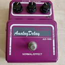 Fialový efekt pedál s nápisem Maxon Analog Delay a označením modelu AD-900. Na horní straně jsou tři černé oválné knoflíky a nápis DC IN.(-)—(+)DC12V…