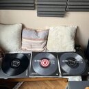Tři vinylové desky v obalech položené na bílém podkladu. Na dvou z nich je viditelný nápis TRAX a SCRATCH, přičemž prostřední disk má červený středov…