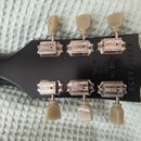 Zadní strana černé hlavy kytary s šesti ladicími kolíky z béžového plastu. Na kovových krytech ladiček je vryto logo GIBSON a nápis DELUXE. Vpravo je…