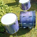 Sada tří bubnů v modré třpytivé barvě s chromovaným kováním. Na basovém bubnu je viditelné logo "Amati". Povrch nástrojů vykazuje známky běžného použ…