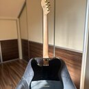Zadní strana kytary s černým bodies a přírodním dřevěným hředcem. Na zadní straně těla je zlatý kovový štít s nápisy „The Milko“, „Handmade in Czech…