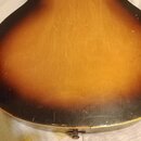 Zadní strana akustické kytary s povrchem v žlutohnatém sunburst provedení. Lak vykazuje četné drobné škrábance a opotřebení, zejména v dolní části ko…