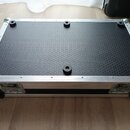 Fotografie znázorňuje spodní stranu černého transportního kufru s hliníkovými hranami a rohy. Povrch dna má strukturovaný včelí vzor a je vybaven šes…