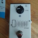 Bílý kytarový pedál s černým ovládacím knoflíkem a kovovým spínacím tlačítkem. Na horní straně jsou nápisy 5V s ikonou USB, 9V a AMP s ikonou zesilov…