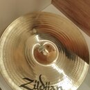 Zlatavý kovový činel s viditelným broušením povrchu. Na spodní části je černý nápis Zildjian. V centru cinchlu je viditelná malá bílá nálepka s nečit…