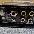 Černý kovový box s nápisy Radial a J33 PHONO DI. Zařízení obsahuje konektory označené jako GROUND Turntable, 1/4"TRS, OUTPUT a PHONO (LEFT, RIGHT), d…